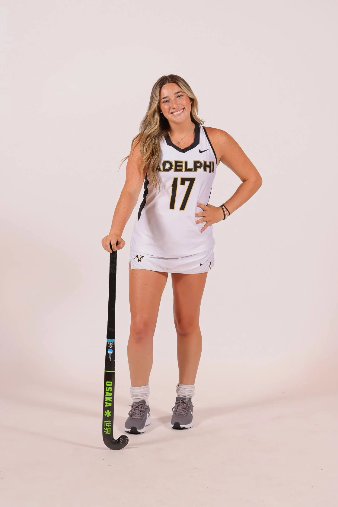 Bella Zullo of Adelphi University standing in her number 17 jersey with a field hockey stick