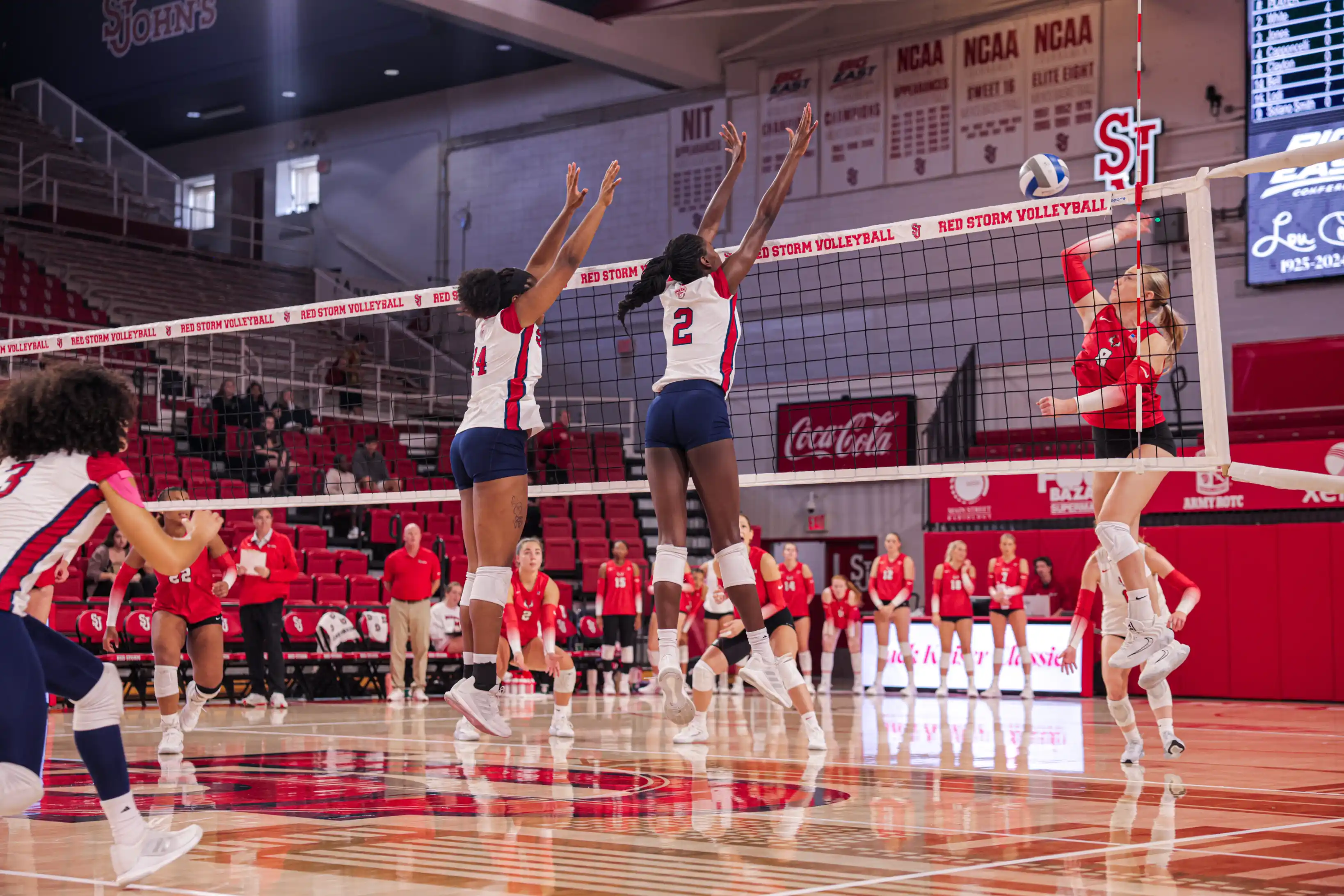 Two volleyball players jumping to block at the net during competitive play